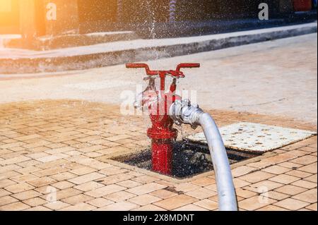 Roter Hydrant mit angeschlossenem Schlauch mit Spritzwasser für die Brandbekämpfung auf dem Bürgersteig in der Stadtstraße im Freien in der Sommernähe Stockfoto