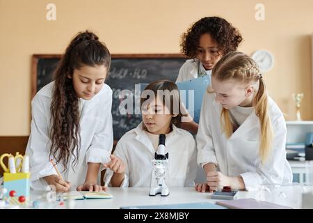 Gruppe von vier ethnisch unterschiedlichen Jungen und Mädchen, die Labormäntel tragen und Chemie in der Schule lernen Stockfoto