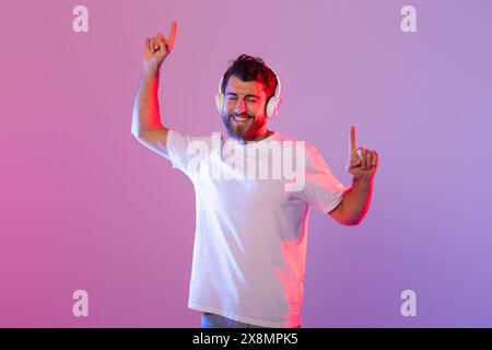 Mann tanzt mit Kopfhörern in farbenfroher Studiobeleuchtung am Abend Stockfoto