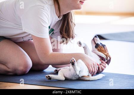 Glückliches Mädchen beim Yoga mit einem kleinen Jack Russell Terrier Welpen im Fitnessstudio. Gesunder Lebensstil und Meditation Stockfoto