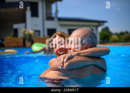 Ein paar fröhliche Senioren rasieren Spaß im Pool mit Freunden, die springen, schwimmen und auf Wagen liegen. Ältere Freunde verbrachten einen heißen Tag am Swimmingpool Stockfoto