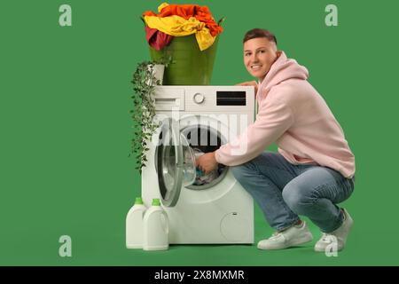 Hübscher junger Mann, der Wäsche in die Waschmaschine auf grünem Hintergrund legt Stockfoto