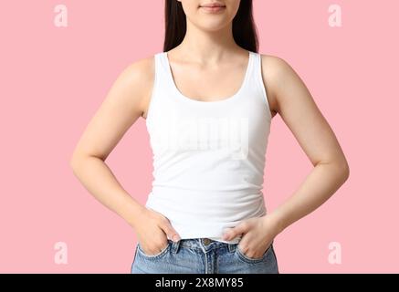 Hübsche junge Frau in stilvollem weißem Tanktop auf rosa Hintergrund Stockfoto