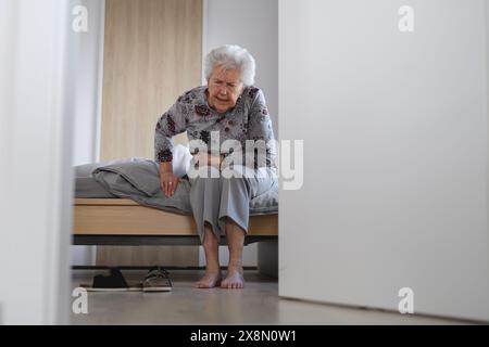 Eine ältere Frau, die versucht, aus dem Bett aufzustehen und Schmerzen spürt. Stockfoto