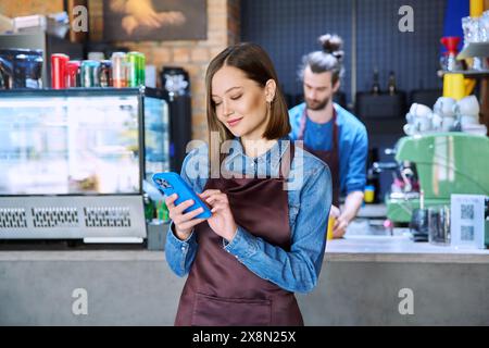 Junge Dienstarbeiterin auf der Schürze mit Smartphone im Restaurant, im Café Stockfoto