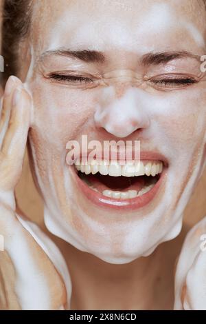 Glückliche moderne 40-jährige Frau mit schäumendem Gesichtsreiniger, der Gesicht wäscht. Stockfoto