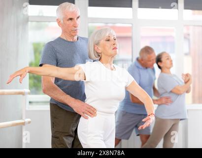 Ältere Tänzerinnen und Tänzer, die während des Trainings verschiedene Ballettbewegungen mit einer Gruppe sportlicher Personen im Trainingsraum ausüben Stockfoto