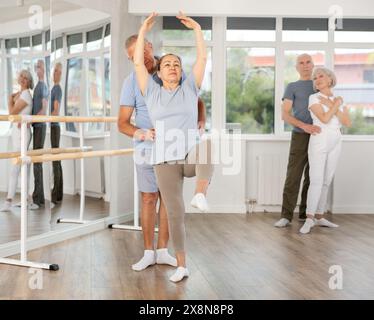 Ältere Tänzerinnen und Tänzer, die während des Trainings verschiedene Ballettbewegungen mit einer Gruppe sportlicher Personen im Trainingsraum ausüben Stockfoto