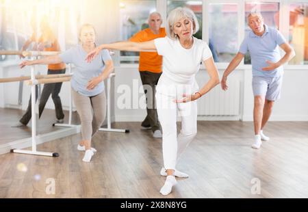 Positive reife Frau, die Ballettpositionen übt und mit anderen in Reihe steht Stockfoto