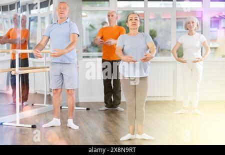 Positive reife Frau, die Ballettpositionen übt und mit anderen in Reihe steht Stockfoto