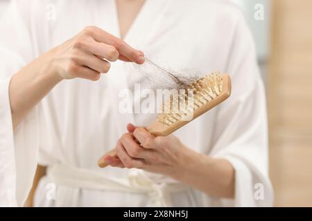 Frau, die ihr verlorenes Haar von der Bürste zu Hause nimmt, Nahaufnahme. Alopezie-Problem Stockfoto