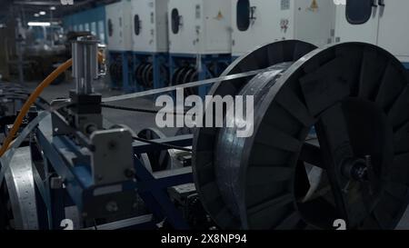 Lange, schmale Metallbleche, die sich auf einer Spule wickeln. Kreativ. Große Spule in einer Fabrikwerkstatt, industrieller Hintergrund. Stockfoto