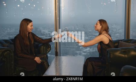 Attraktive Frauen zwitschern Gläser und trinken Champagner im Restaurant. Medien. Schöne junge Frauen entspannen sich im Champagnerrestaurant. Freunde treffen sich und Stockfoto