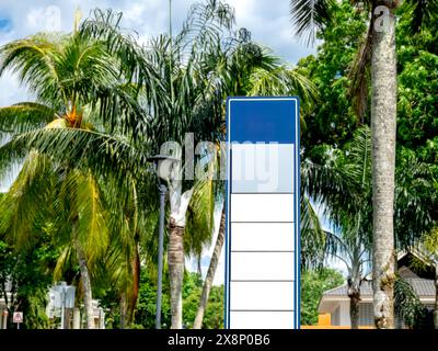 Leeres weißes und blaues leeres Banner oder Straßenschild für Werbung neben der Straße in der Nähe der Palmen und des grünen Gartens. Modell hoch und hoch für den Außenbereich Stockfoto