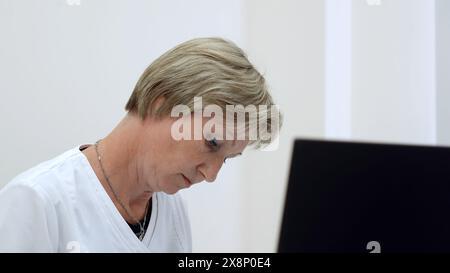 Frau mittleren Alters, die in der Klinik arbeitet. Clip. Arzt oder Krankenschwester arbeiten mit Papieren vor dem Computer. Stockfoto