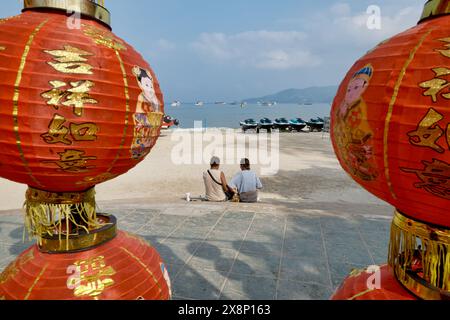 Zwischen zwei roten chinesischen Laternen sitzen ein paar Touristen am Patong Beach, Patong, Südthailand Stockfoto