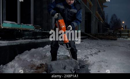 Man bohrt Löcher in einen Betonblock. Clip. Industrieller Hintergrund eines Baumeisters auf der Baustelle. Stockfoto