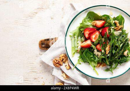Löwenzahn-Salat mit Erdbeere und Wallnüssen in Teller auf weißem Hintergrund, Blick von oben. Stockfoto