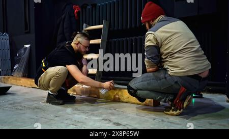 Spritzlackierung von Holzbalken in einem Konzertsaal. Medien. Junger Mann, der Holzbalken mit schwarzer Farbe dekoriert. Stockfoto