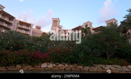 Blick von einem kleinen Teich auf wunderschöne blühende Büsche mit rosa Blumen. Aktion. Grüne Vegetation und Luxuswohnung dahinter. Stockfoto