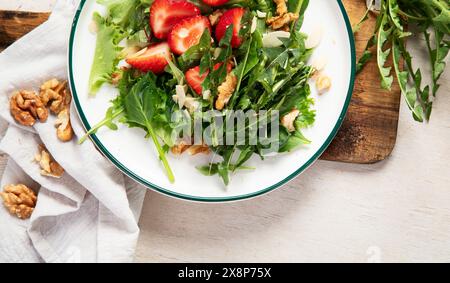 Löwenzahn-Salat mit Erdbeere und Wallnüssen in Teller auf weißem Hintergrund, Blick von oben. Panorama mit Kopierbereich. Stockfoto