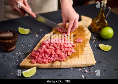 Frau Schnitt Thunfischsteak in Scheiben auf einem hölzernen Schneidebrett in der Hausküche Stockfoto