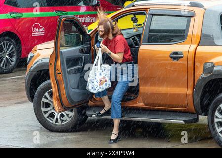 SAMUT PRAKAN, THAILAND, 7. MAI 2024, Eine Frau mit fließenden Haaren steigt aus einem Auto auf einer windigen Straße Stockfoto