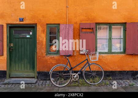 In diesem Bild erwacht eine malerische europäische Straße zum Leben, in der sich ein Vintage-Fahrrad mit einem Korb an eine orangene Wand lehnt Stockfoto