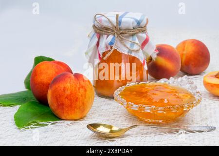 Pfirsichenmarmelade auf dem Tisch in einem Glas, neben einer Schüssel mit Marmelade und Löffeln, Pfirsiche Stockfoto