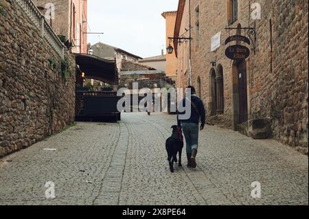 Eine Person und ein Hund gehen auf einem Kopfsteinpflasterweg. Flankiert von historischen Steinhäusern in dieser rustikalen mittelalterlichen Straße. Stockfoto