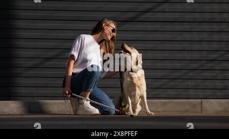 Eine blinde Frau geht mit ihrem Blindenhund auf die Straße. Ein Mädchen, das einen labrador umarmt. Stockfoto