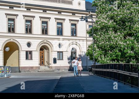 Ein Paar, das an einem sonnigen Frühlingstag in Norrköping, Schweden, an einem blühenden Kastanienbaum auf der Gamlebro-Brücke über den Motala-Fluss vorbeispaziert. Stockfoto
