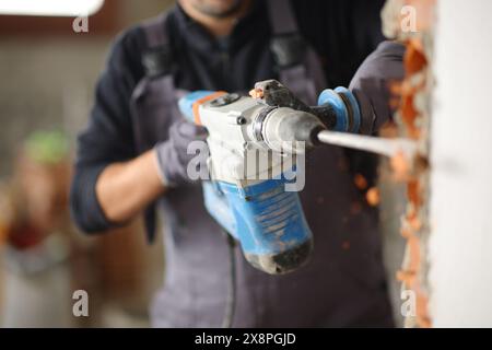 Nahaufnahme eines Bauarbeiters, der einen Bohrhammer benutzt, um die Mauer in einem Haus zu zerstören, das gerade renoviert wird Stockfoto