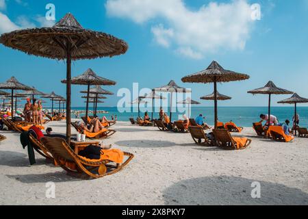 Sir Bani Yas, VAE - 5. Januar 2024: Touristen genießen einen sonnigen Tag an den unberührten weißen Stränden unter malerischen Strohschirmen. Stockfoto