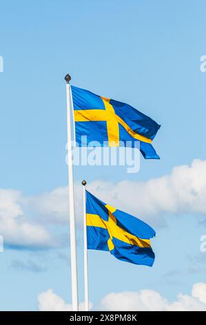 Zwei schwedische Fahnen flattern an einem sonnigen Tag in der Brise und erzeugen eine patriotische Darstellung vor dem blauen Himmel. Stockfoto