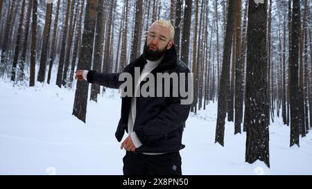 Porträt eines hübschen jungen bärtigen Mannes in warmer Kleidung, der draußen im Park am Wintertag steht. Medien. Hipster-blondes Modell im Wald. Stockfoto