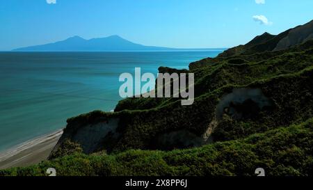 Felsen einer unbewohnten Insel im Mittelmeer. Clip. Bewaldete grüne Hügel und blaues Meer mit wolkenlosem Horizont im Hintergrund. Stockfoto