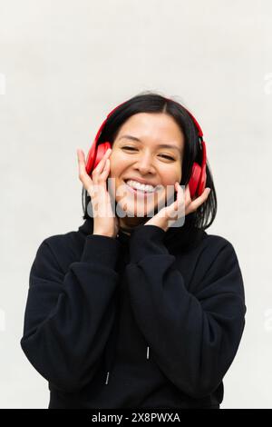 Das Porträt einer jungen Frau in schwarzer Kleidung und Kopfhörern singt fröhlich zur Musik mit, mit einem hellen und fröhlichen Ausdruck auf ihrem Gesicht. Stockfoto