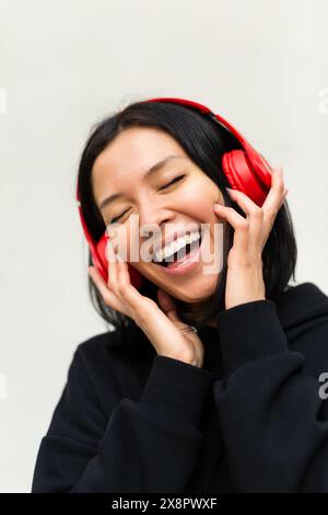 Das Porträt einer jungen Frau in schwarzer Kleidung und Kopfhörern singt fröhlich zur Musik mit, mit einem hellen und fröhlichen Ausdruck auf ihrem Gesicht. Stockfoto