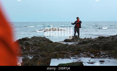 Die Frau tanzt auf Felsen im Wasser des Meeres. Clip. Die Frau tanzt glücklich auf Felsen am Meer. Lustige Frau, die auf felsigen Felsen des Meeres tanzt Stockfoto