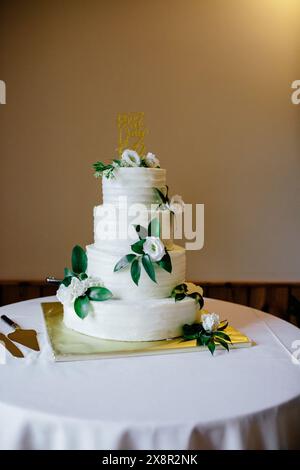 Dreistufige weiße Hochzeitstorte mit grünen Blättern, weißen Blumen Stockfoto