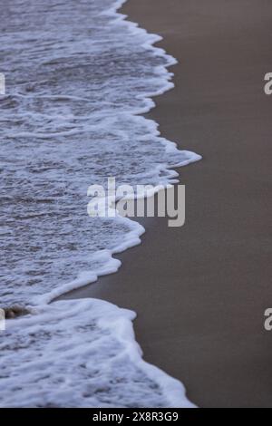 Sanfte Meeresschaumkrone auf weißer Welle trifft auf beigefarbenen Sandstrand Stockfoto