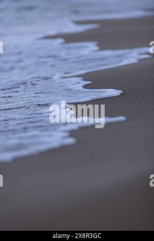 Sanfte Meeresschaumkrone auf weißer Welle trifft auf beigefarbenen Sandstrand Stockfoto