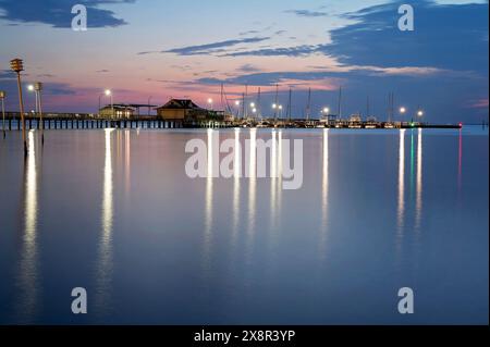 Abendlicher Blick auf einen beleuchteten Pier und Yachthafen, der sich auf ruhigem Wasser spiegelt Stockfoto