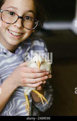 Ein lächelndes Mädchen in einer Brille hält die gelbe Küken zu Hause Stockfoto