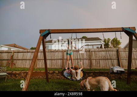 Kinder und Hund spielen draußen auf dem Schaukel-Set mit Rainbow Stockfoto