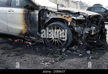 Ein vollständig ausgebranntes Fahrzeug, Ansicht der vorderen rechten Seite des Fahrzeugs mit schwarzen Brandspuren auf der weißen Farbe und verbranntem Motorraum. Stockfoto