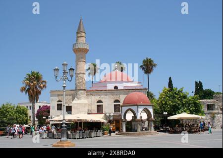 KOS, GRIECHENLAND-19. JULI 2013: Unbekannte Touristen, die an einem heißen Sommertag an der berühmten Moschee aus der osmanischen Ära vorbeispazieren Stockfoto