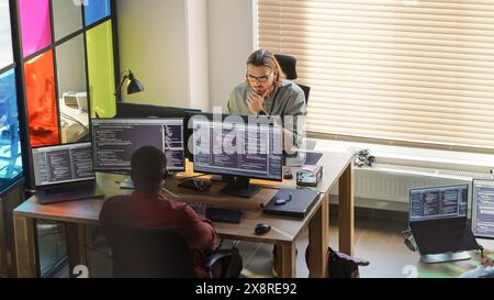 Verschiedene Kollegen schreiben Code auf Desktop-Computern mit Professional Multiple Monitors Setup. Softwareentwicklungsabteilung, die an der Software-as-a-Service-Plattform für Geschäftskunden arbeitet. Stockfoto