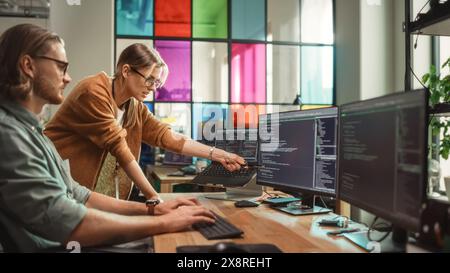 Weibliche Senior Software Engineer berät männliche Junior Developer und zeigt auf Desktop Computer Display mit Code. Kaukasische Frau bietet neue Funktionen und hilft bei der Behebung von Fehlern in der modernen SaaS-Plattform. Stockfoto